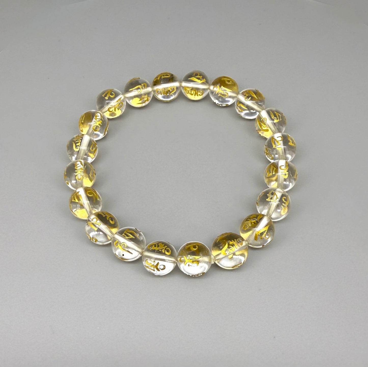 Clear quartz beaded bracelet, 19cm, transparent gemstone beads engraved with golden Sanskrit mantra Om Mani Padme Hum on elastic stretch band.
