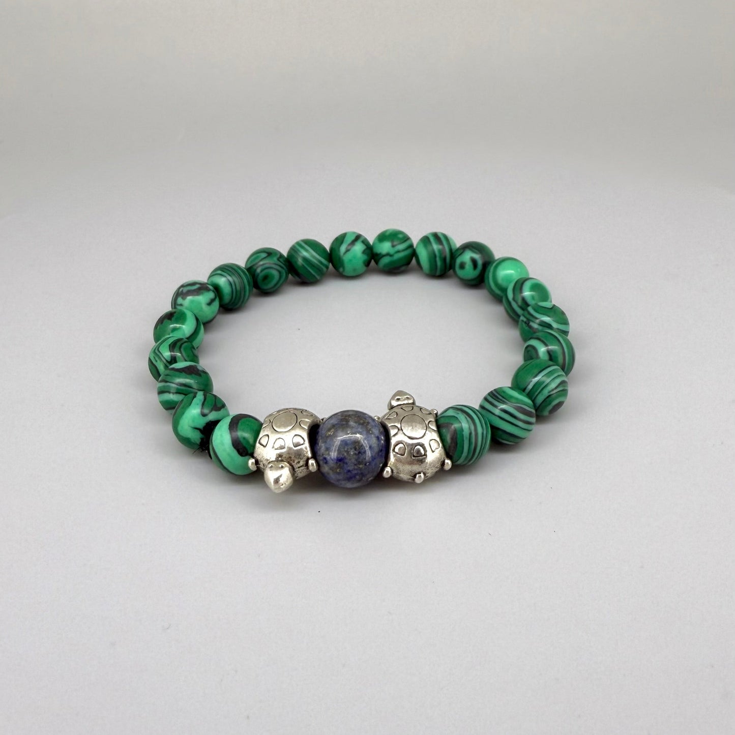 Malachite beaded bracelet, 18cm, green gemstone beads with central blue bead framed by two metal turtle accents on elastic stretch band.