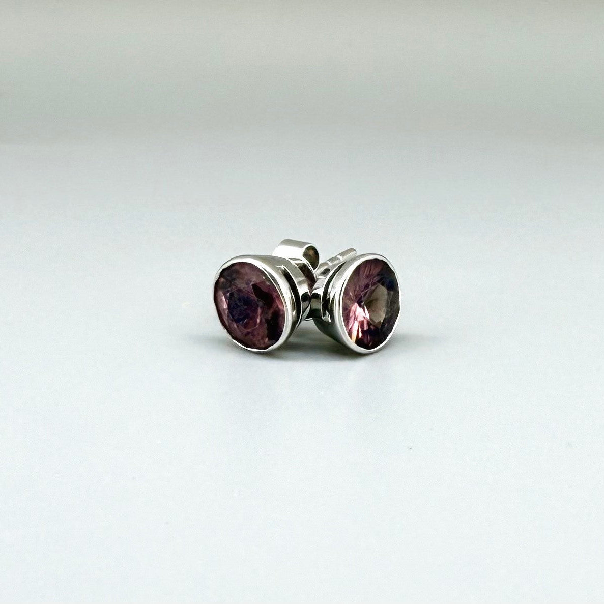 White gold stud earrings featuring round-cut rhodolite garnets in a classic setting.