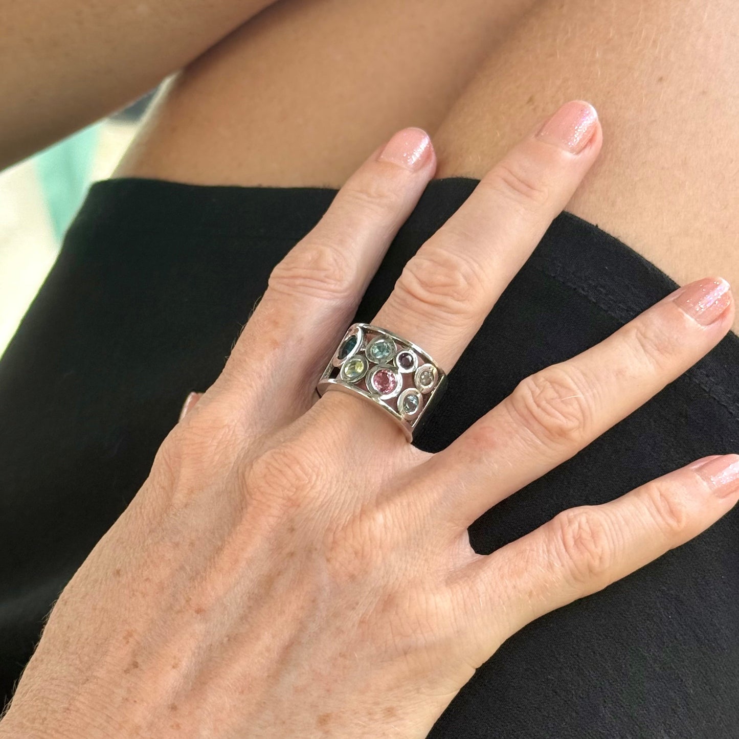 Multicolor sapphire band ring in white gold plated sterling silver, featuring faceted blue, yellow, pink, and green gemstones in elegant wide band design.