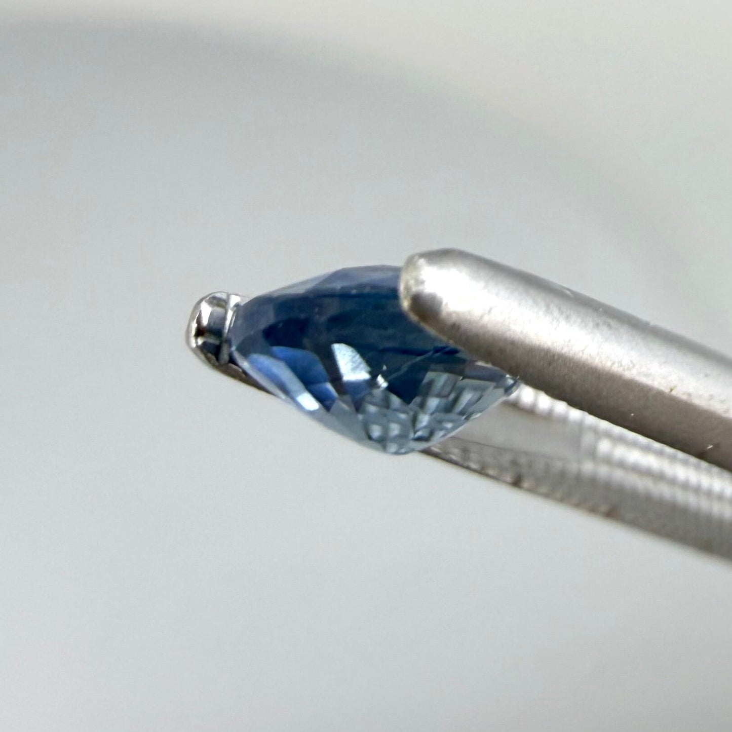 0.84 ct natural bright-blue sapphire from Bangkaja, oval cut, shown held with tweezers.