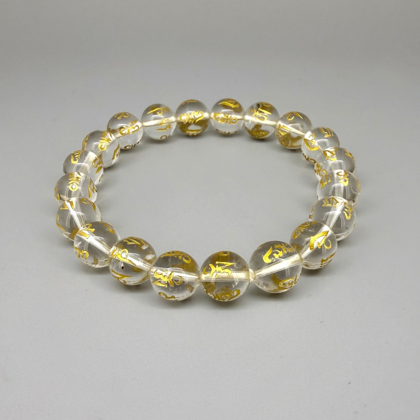 Clear quartz beaded bracelet, 19cm, transparent gemstone beads engraved with golden Sanskrit mantra Om Mani Padme Hum on elastic stretch band.