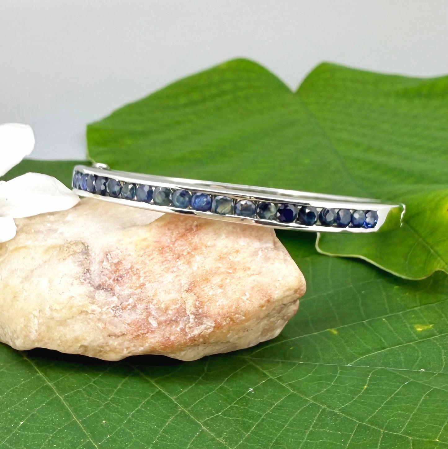 Blue sapphire bangle in white gold plated sterling silver with faceted deep blue gemstones.