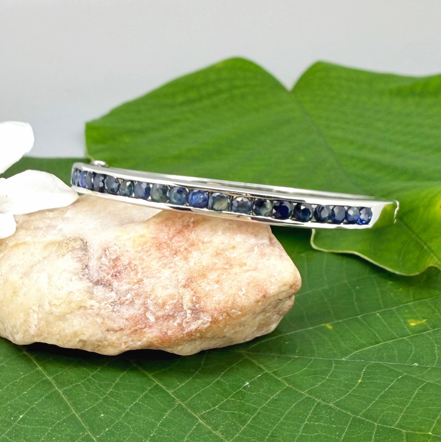 Blue sapphire bangle in white gold plated sterling silver with faceted deep blue gemstones.