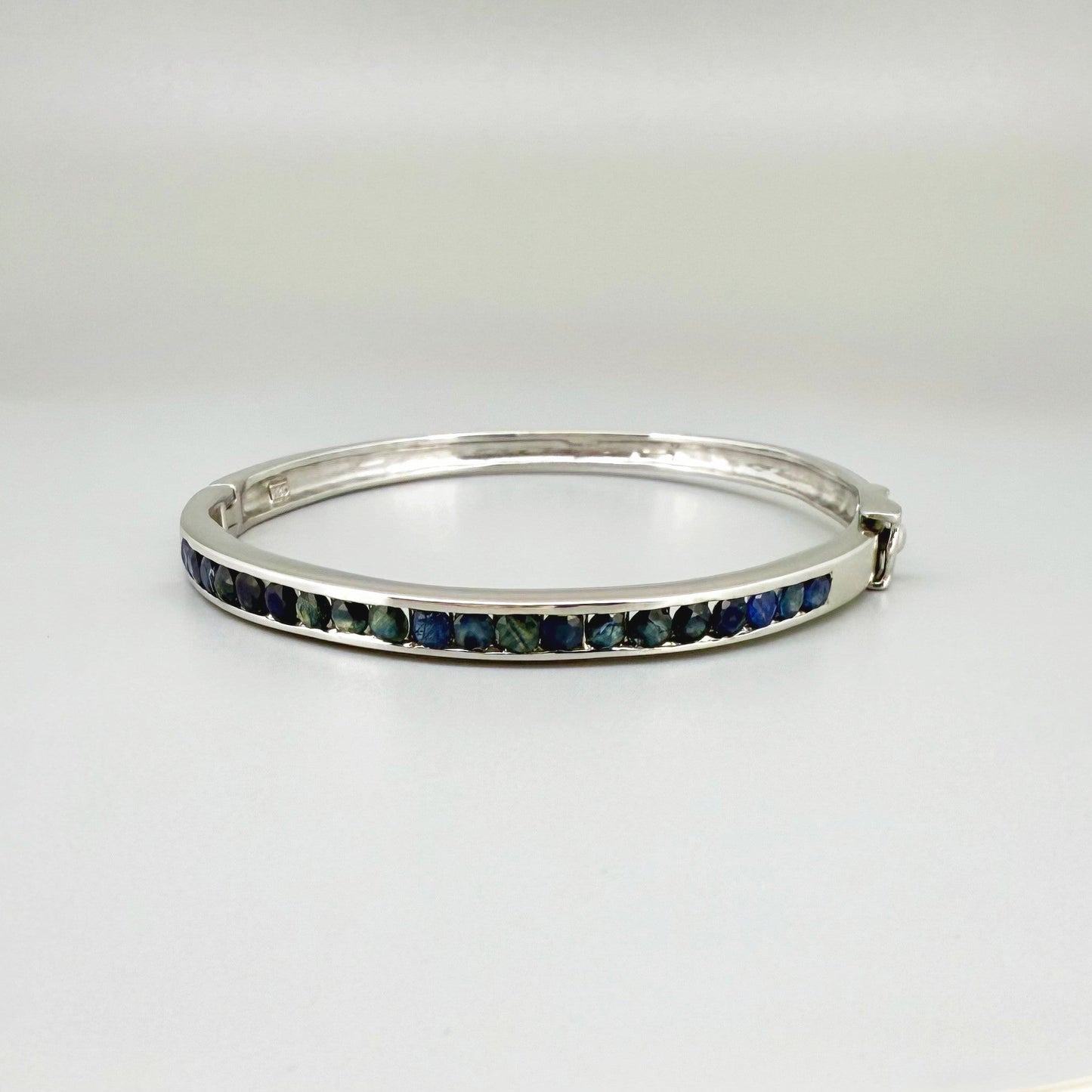 Blue sapphire bangle in white gold plated sterling silver with faceted deep blue gemstones.