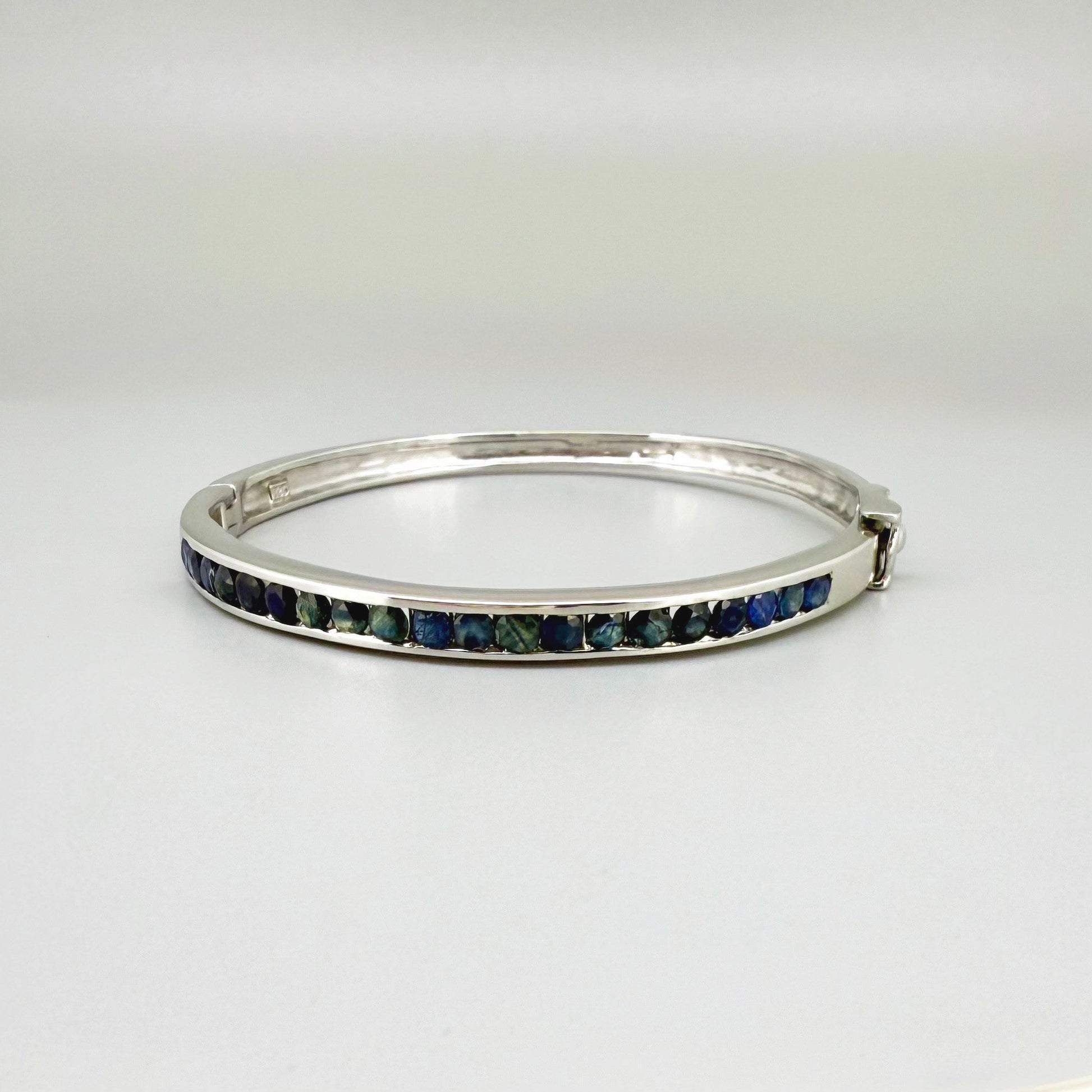 Blue sapphire bangle in white gold plated sterling silver with faceted deep blue gemstones.