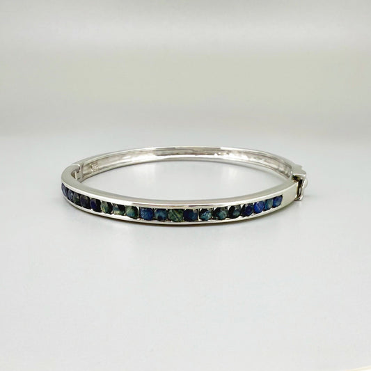 Blue sapphire bangle in white gold plated sterling silver with faceted deep blue gemstones.