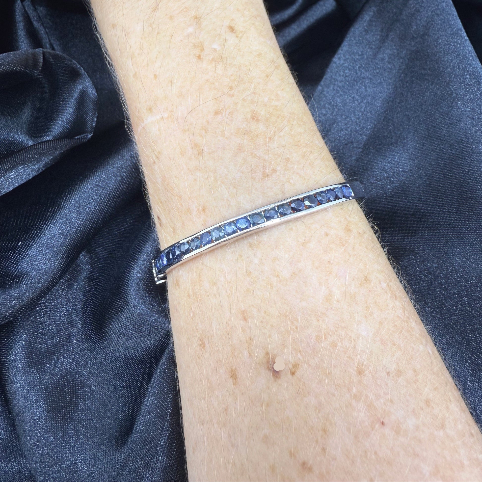 Blue sapphire bangle in white gold plated sterling silver with faceted deep blue gemstones.