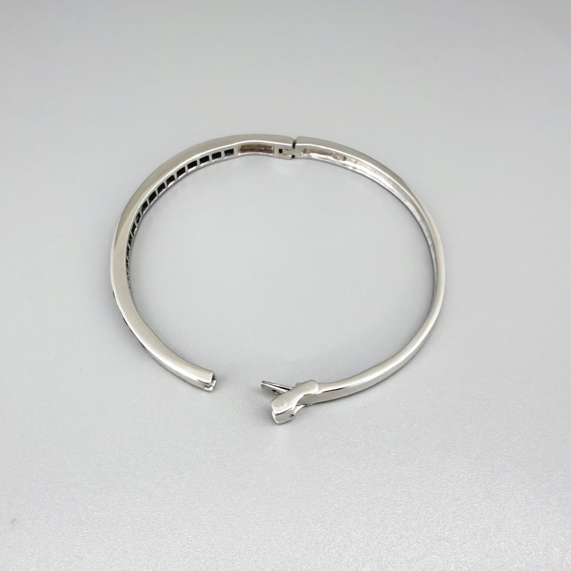 Blue sapphire bangle in white gold plated sterling silver with faceted deep blue gemstones.
