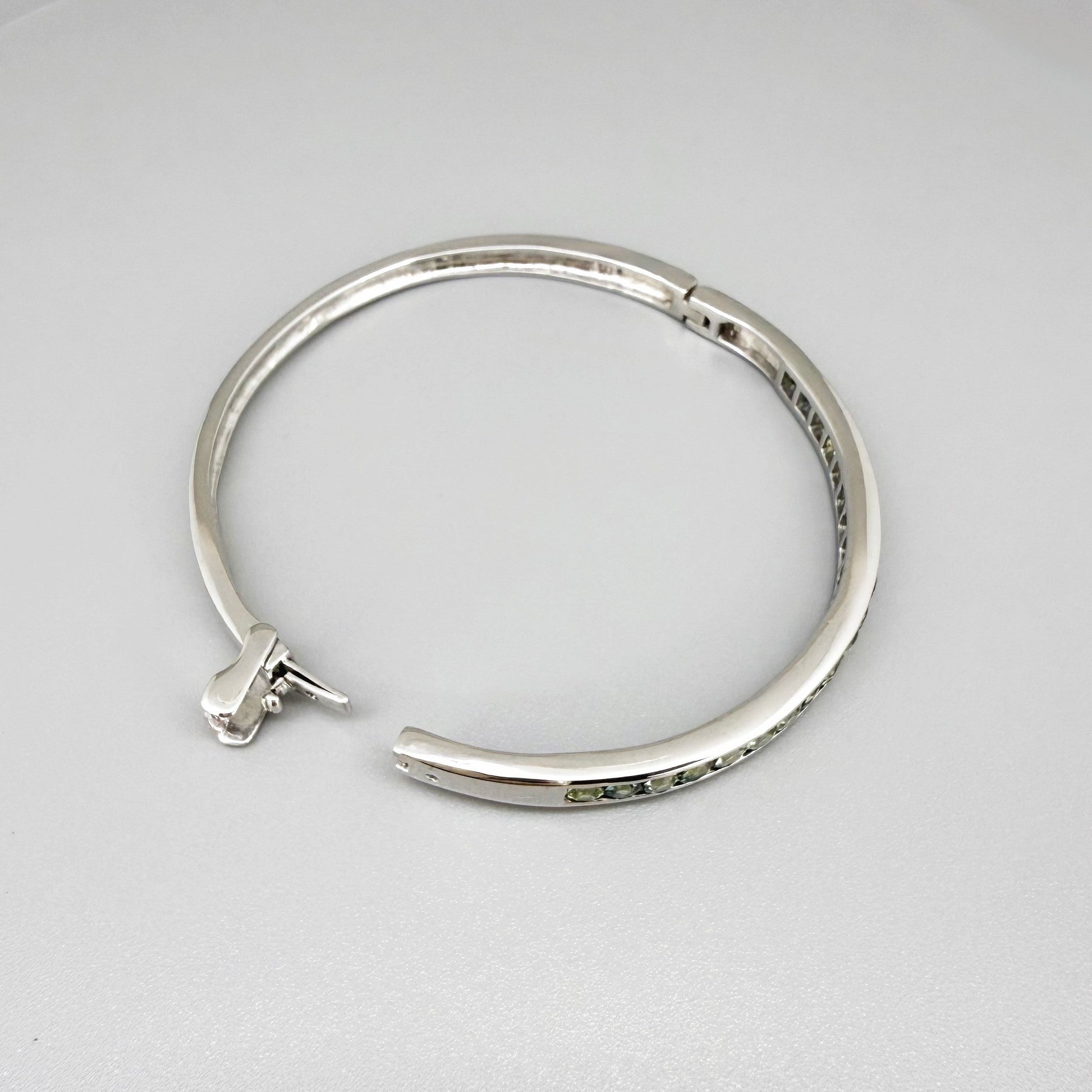 White gold plated silver bangle set with faceted natural green sapphires.