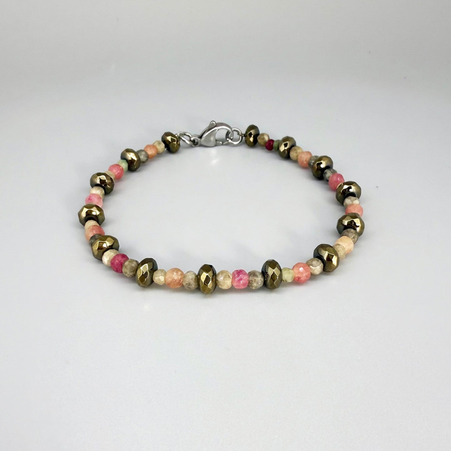 Faceted beaded bracelet with ruby, sapphire, emerald, and pyrite gemstones on neutral background