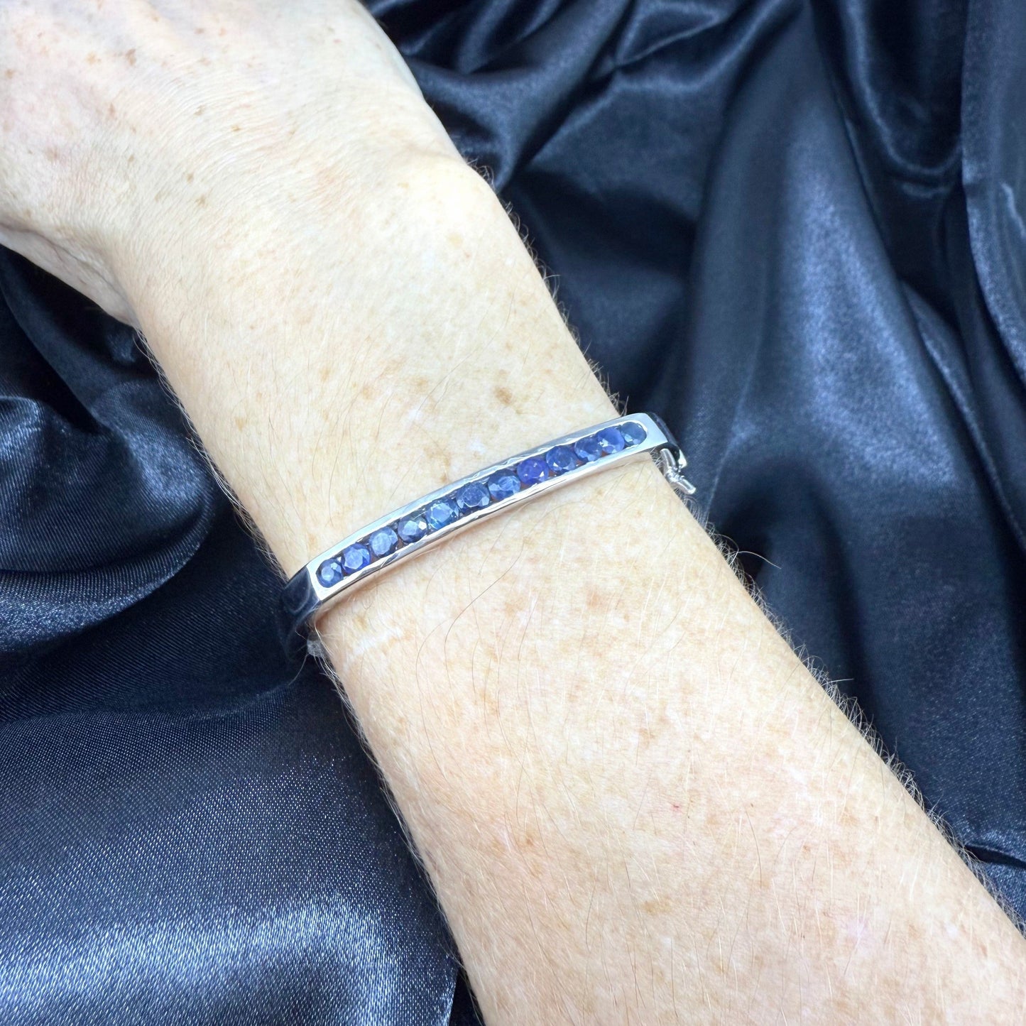 White gold plated silver bangle with natural blue sapphires in a sleek classic design.