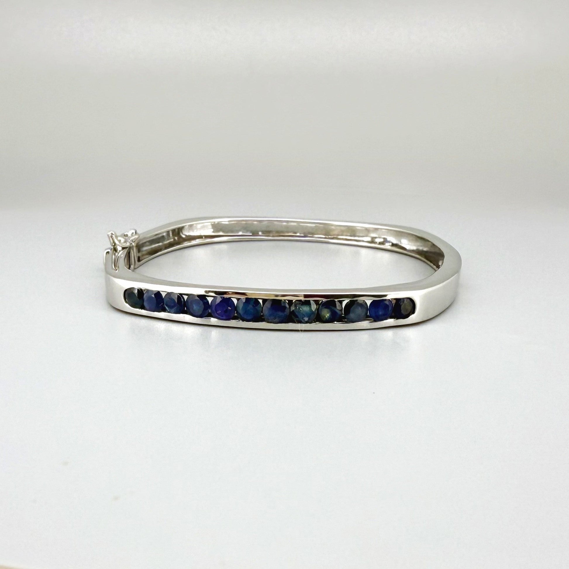 White gold plated silver bangle with natural blue sapphires in a sleek classic design.