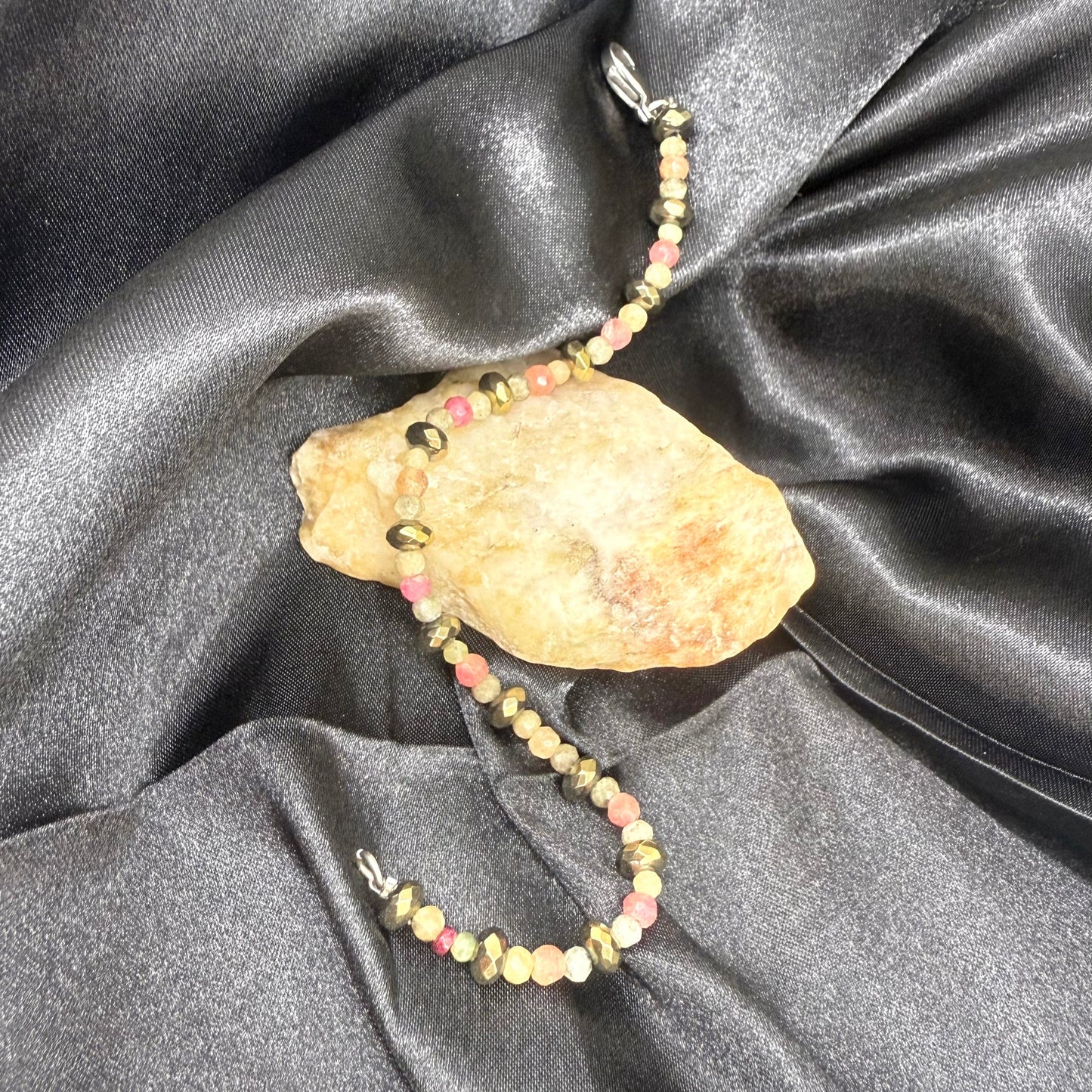 Faceted beaded bracelet with ruby, sapphire, emerald, and pyrite gemstones on neutral background