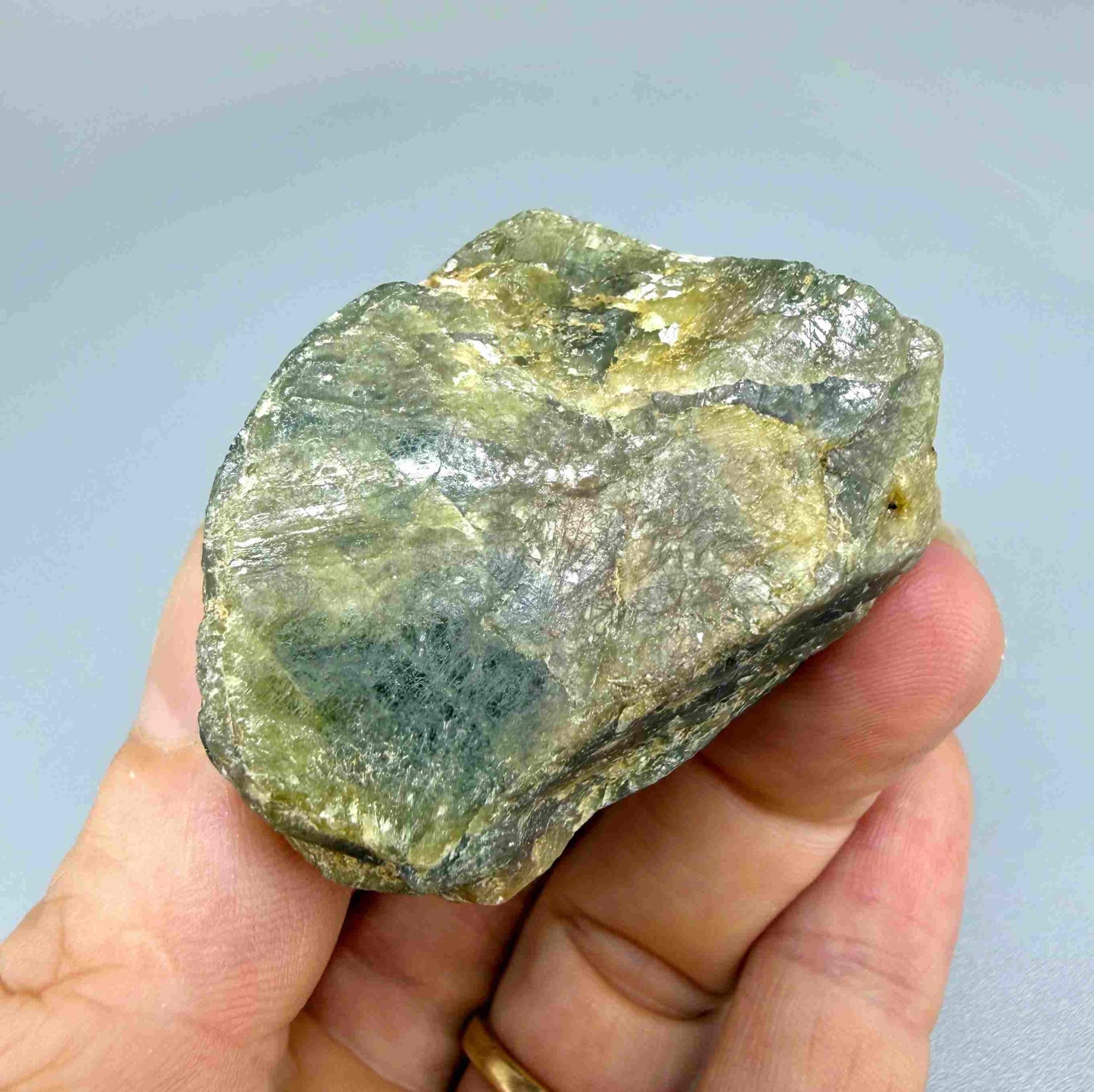 Natural rough green sapphire, opaque and uncut, showing olive to yellow-green tones, photographed on neutral background.