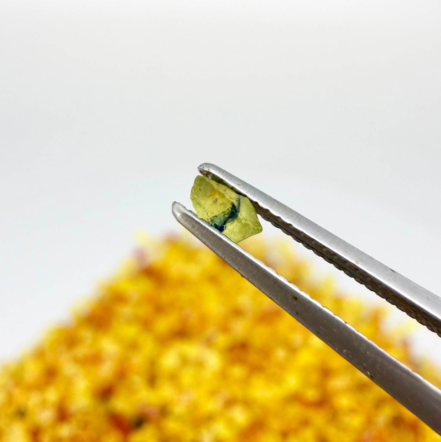 Natural sapphire rough with warm yellow-orange hues and subtle color variation, uncut corundum photographed on neutral background.