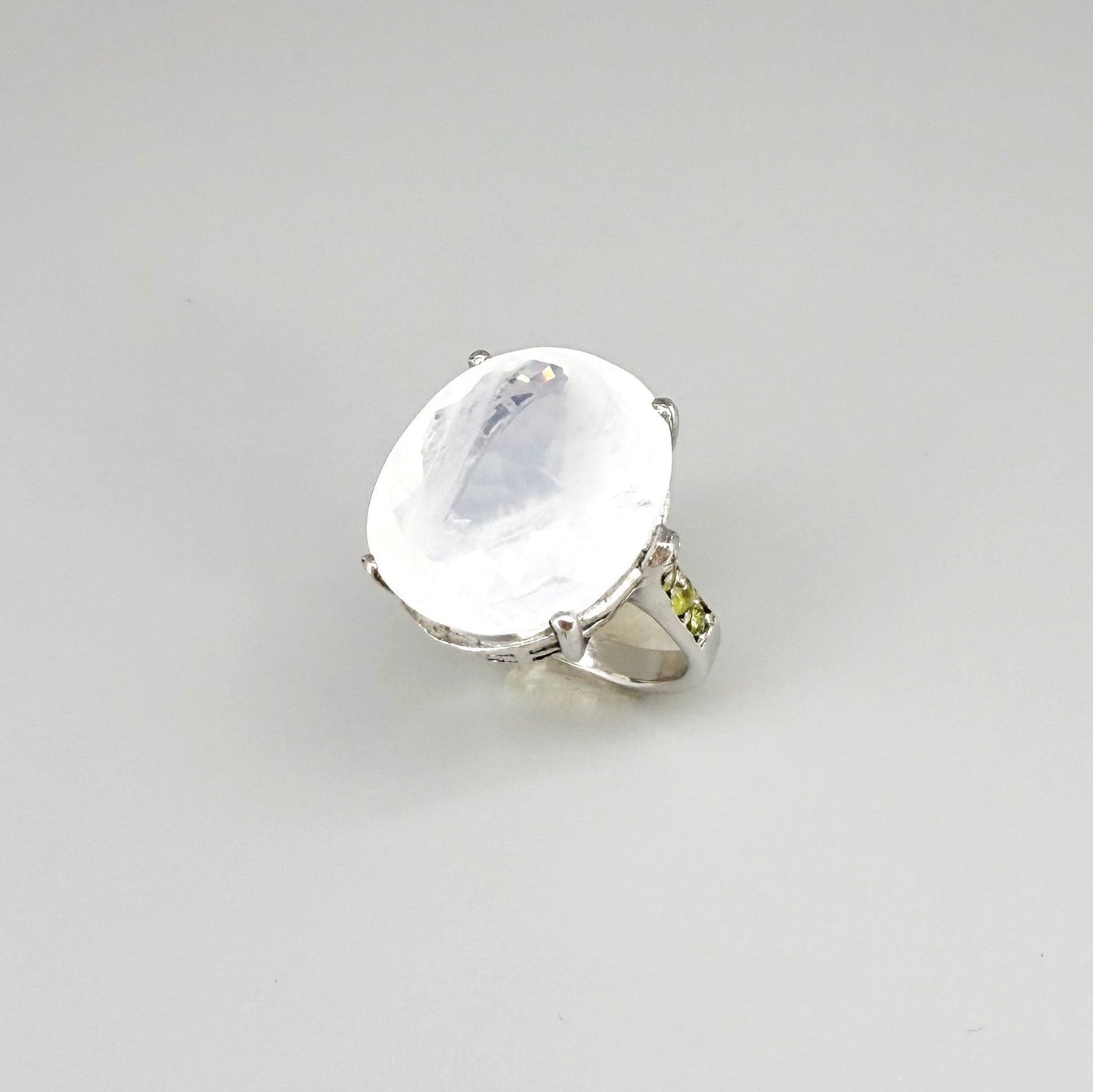 White quartz and sapphire ring in white gold plated sterling silver, featuring a faceted clear gemstone framed by blue sapphires, elegant and refined design.