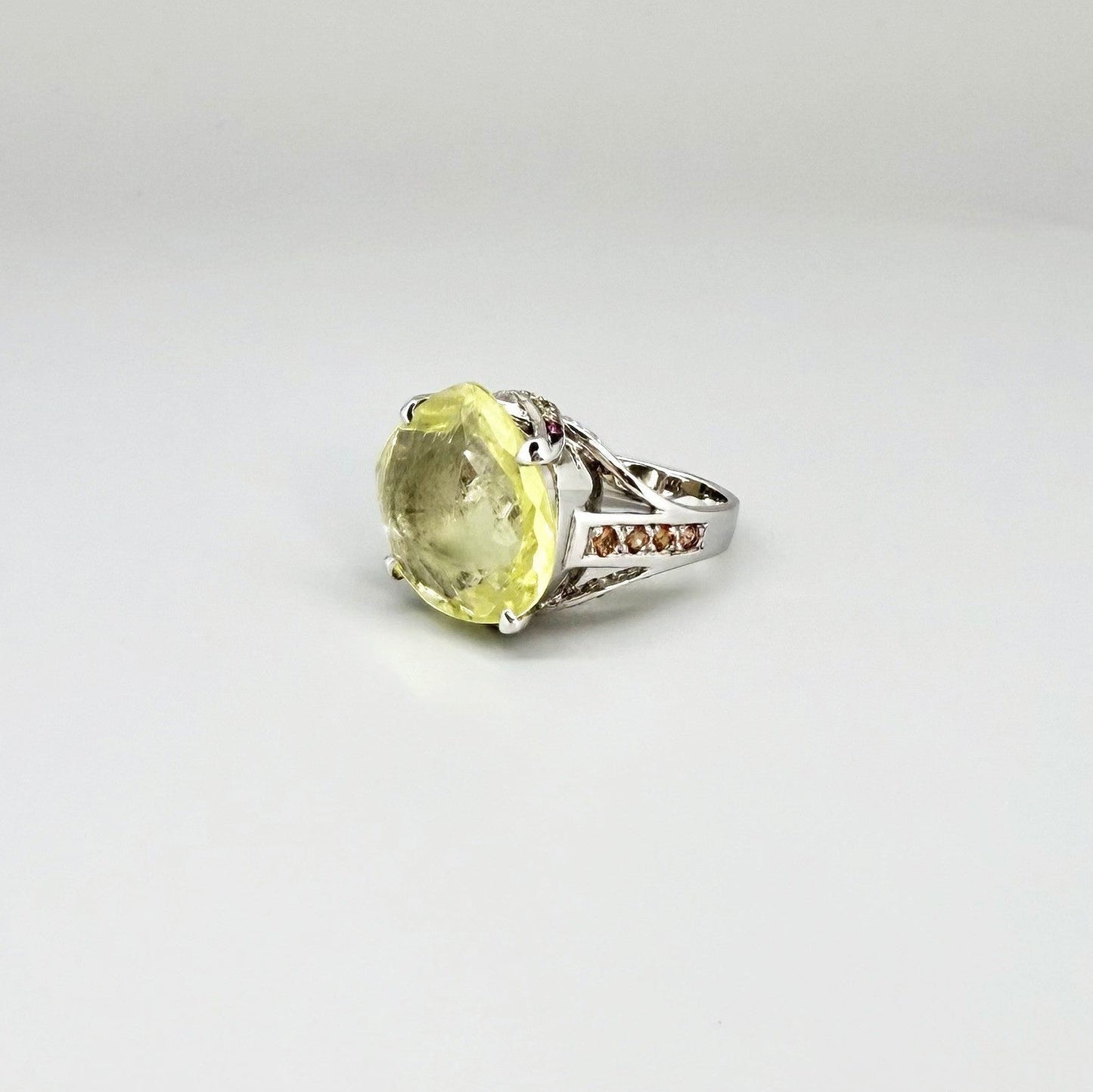 White gold plated sterling silver ring featuring a lemon quartz gemstone surrounded by orange sapphires in a halo design.