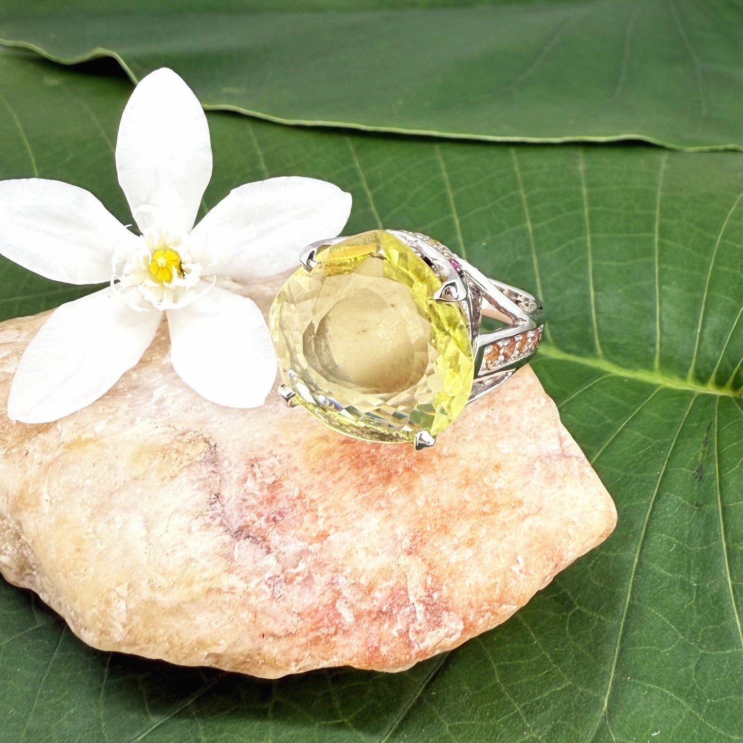 White gold plated sterling silver ring featuring a lemon quartz gemstone surrounded by orange sapphires in a halo design.