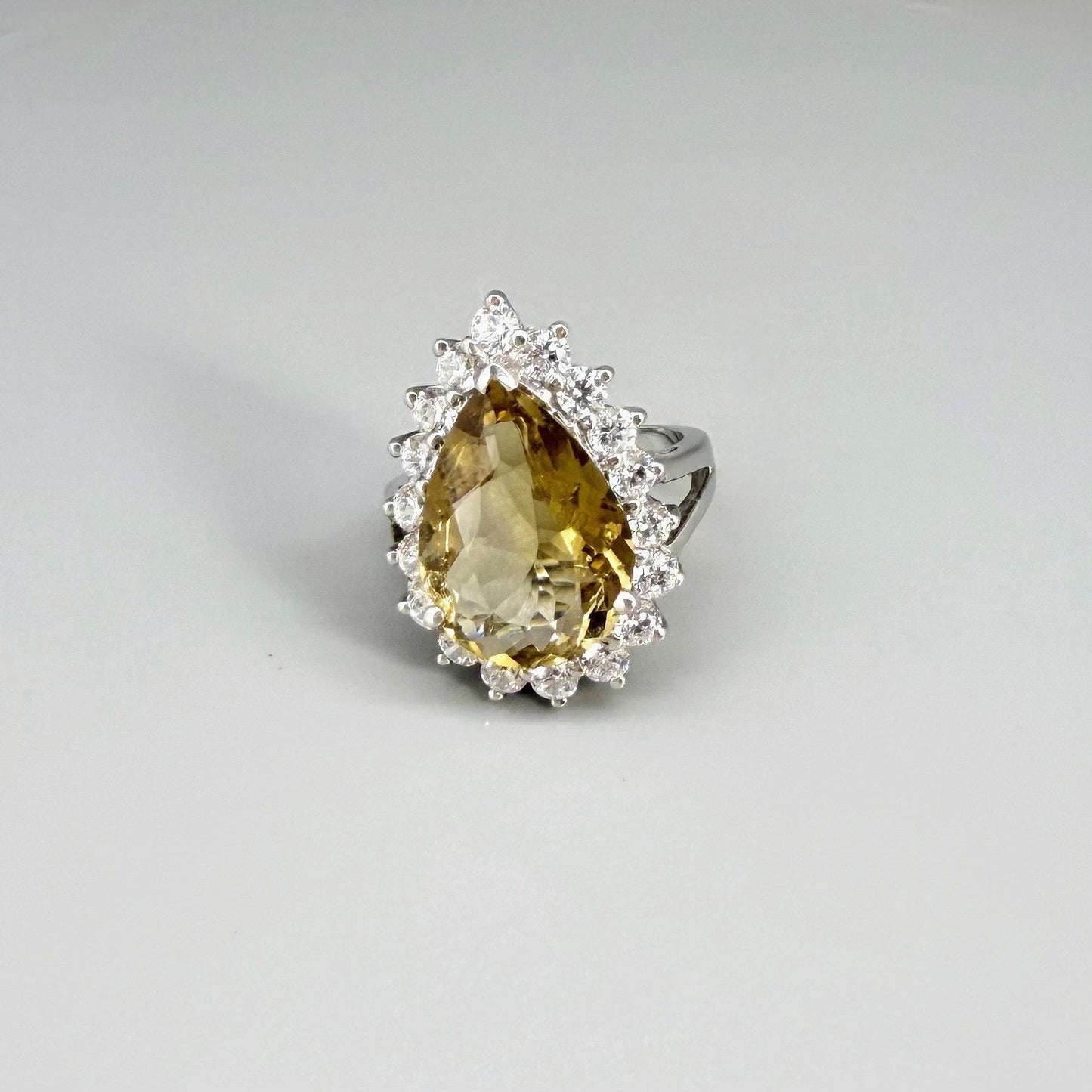 Citrine and CZ ring in white gold plated sterling silver, featuring a pear-shaped golden-yellow gemstone surrounded by clear cubic zirconia halo, elegant and refined design