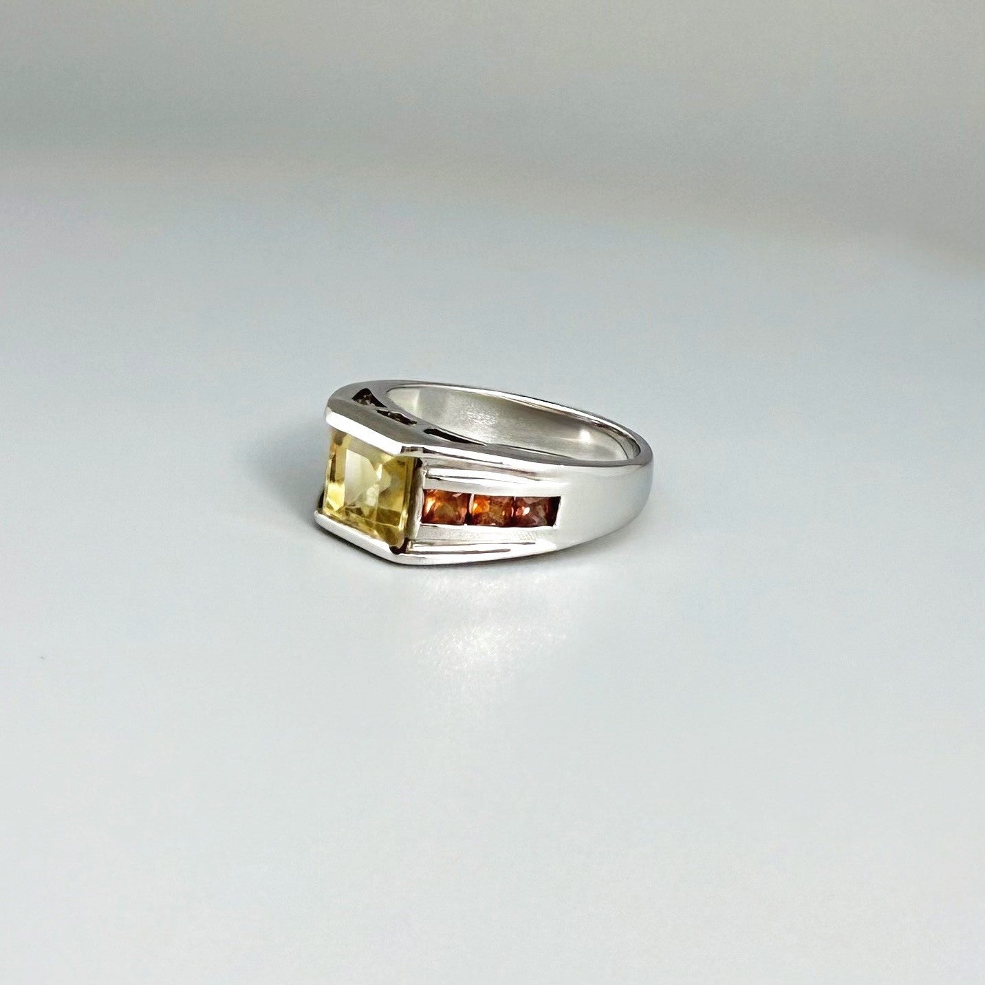 Citrine and sapphire ring in white gold plated sterling silver, featuring a rectangular golden-yellow gemstone flanked by orange sapphires, elegant and timeless design.