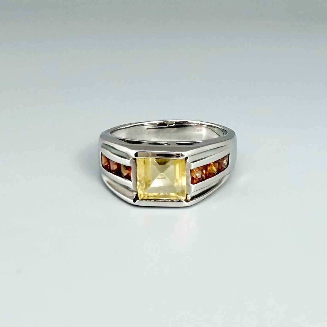 Citrine and sapphire ring in white gold plated sterling silver, featuring a rectangular golden-yellow gemstone flanked by orange sapphires, elegant and timeless design.