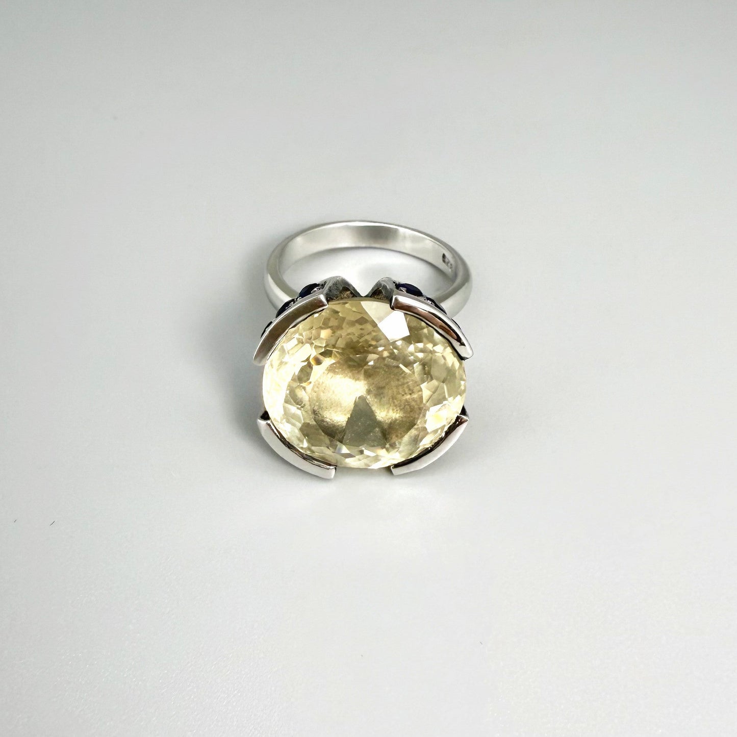 Lemon quartz and sapphire ring in white gold plated sterling silver, featuring a faceted yellow-green gemstone framed by deep blue sapphires, elegant and vibrant design.