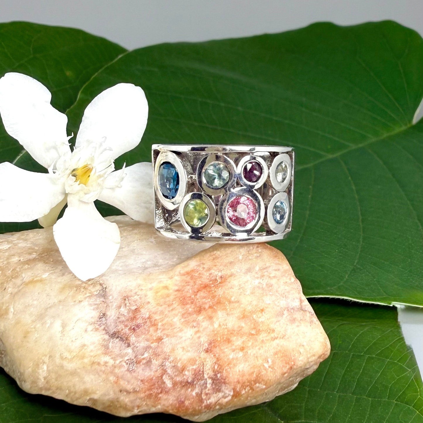 Multicolor sapphire band ring in white gold plated sterling silver, featuring faceted blue, yellow, pink, and green gemstones in elegant wide band design.