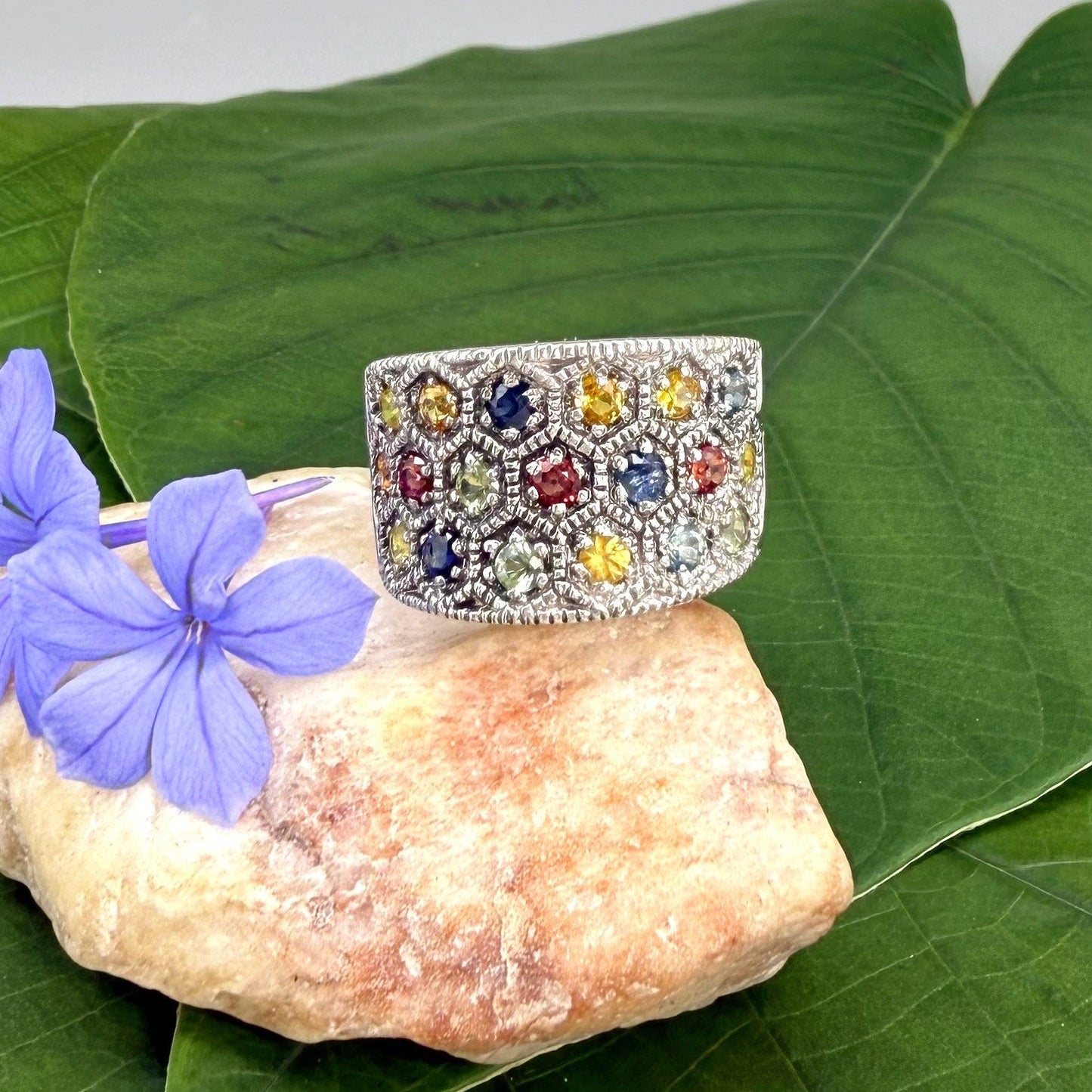 Multicolor sapphire band ring in white gold plated sterling silver, featuring faceted blue, yellow, pink, green, and orange gemstones, elegant wide design.