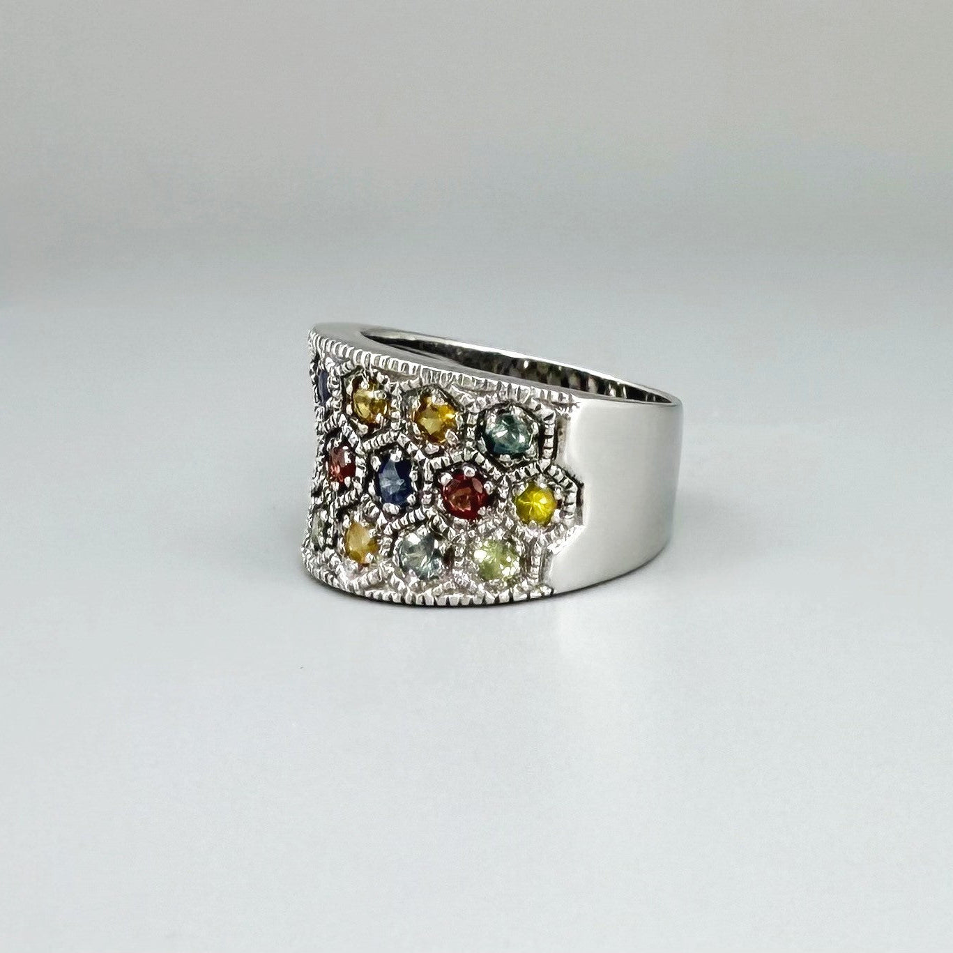 Multicolor sapphire band ring in white gold plated sterling silver, featuring faceted blue, yellow, pink, green, and orange gemstones, elegant wide design.