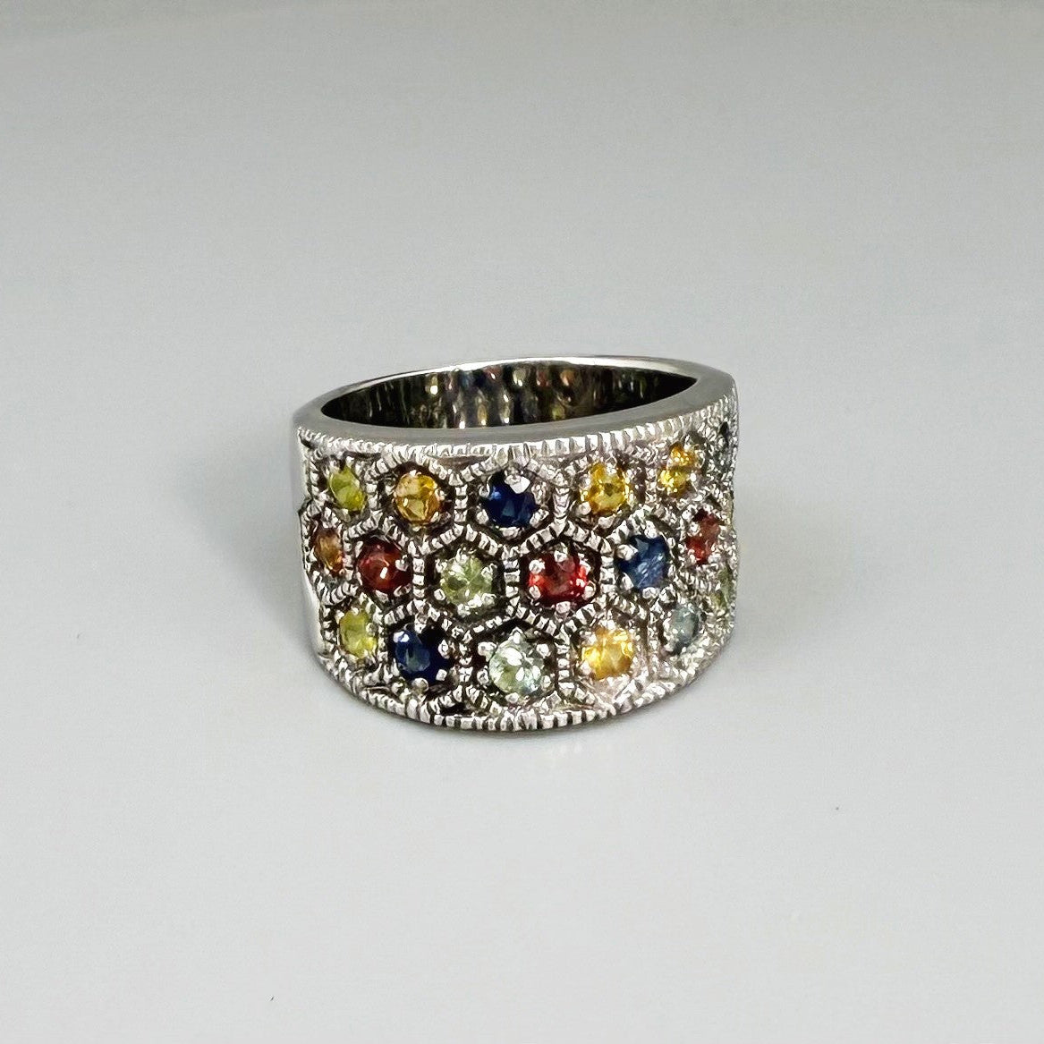Multicolor sapphire band ring in white gold plated sterling silver, featuring faceted blue, yellow, pink, green, and orange gemstones, elegant wide design.