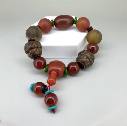Carnelian and agate beaded bracelet, 20cm, orange-red and brown gemstone beads with two carved wooden head accents on elastic stretch band.