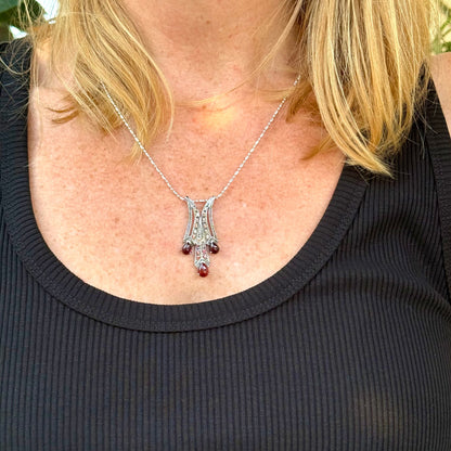 Person wearing a necklace with a decorative pendant with Garnet Gemstones and Fancy Sapphires