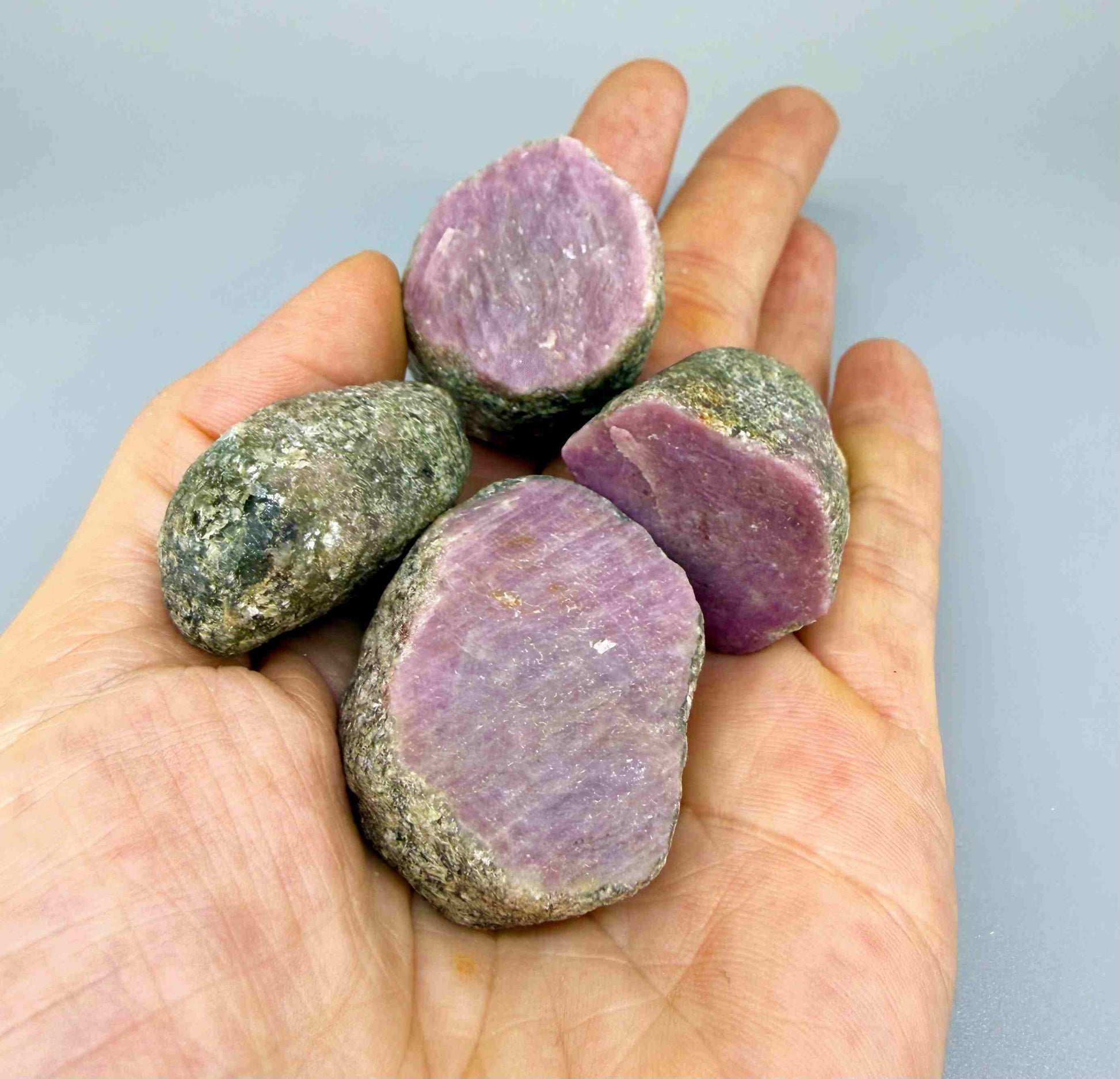 Natural ruby in grey-green host rock, uncut rough stones with pink to purplish-pink ruby sections.