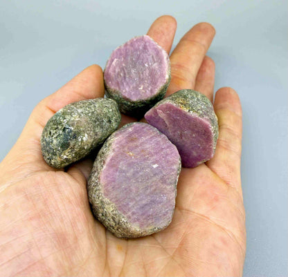 Natural ruby in grey-green host rock, uncut rough stones with pink to purplish-pink ruby sections.