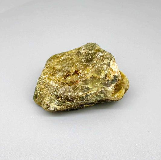 Natural rough green sapphire, opaque and uncut, showing olive to yellow-green tones, photographed on neutral background.