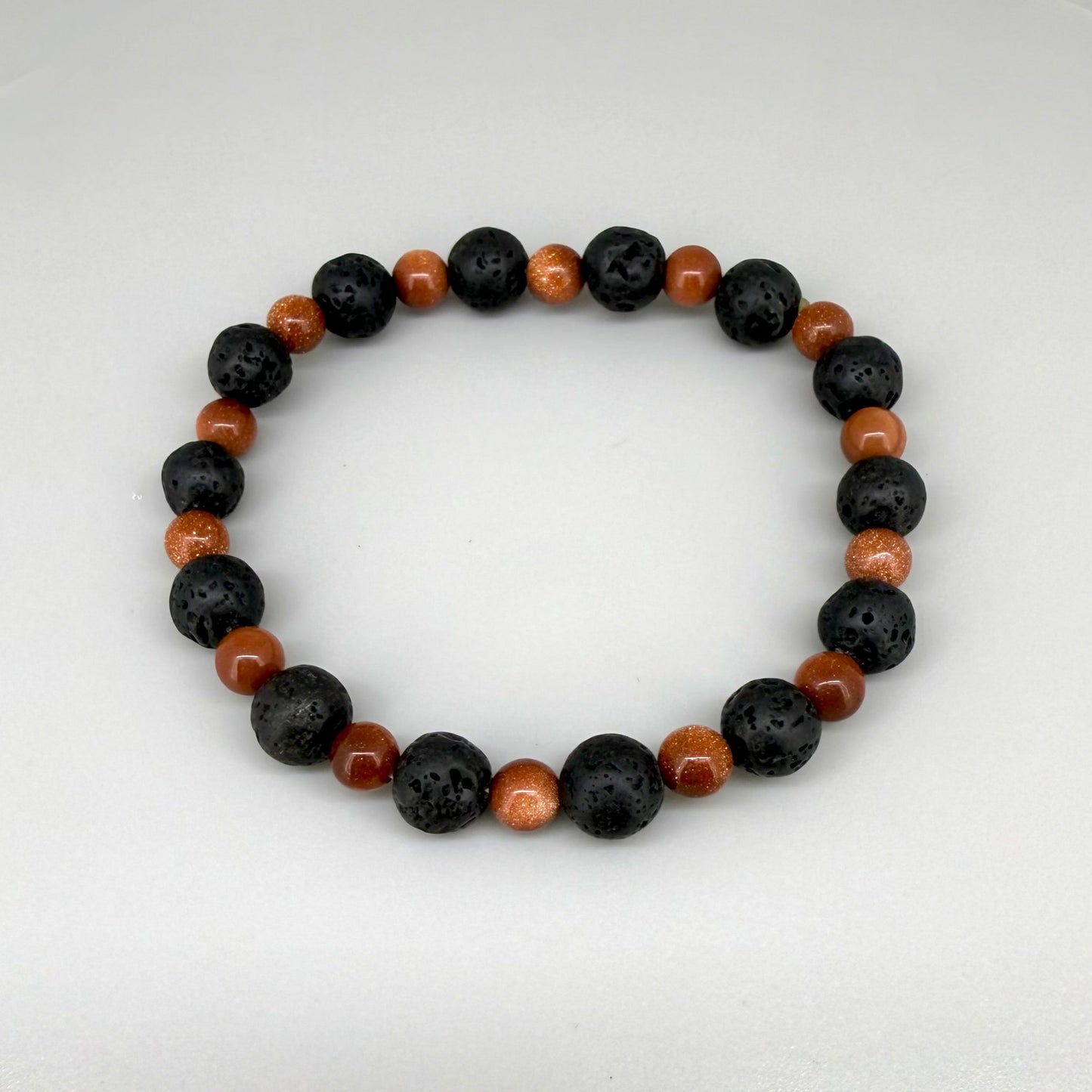 Lava and goldstone beaded bracelet, 18cm, alternating matte black lava beads and smaller shimmering golden-brown man-made goldstone beads on elastic stretch band.