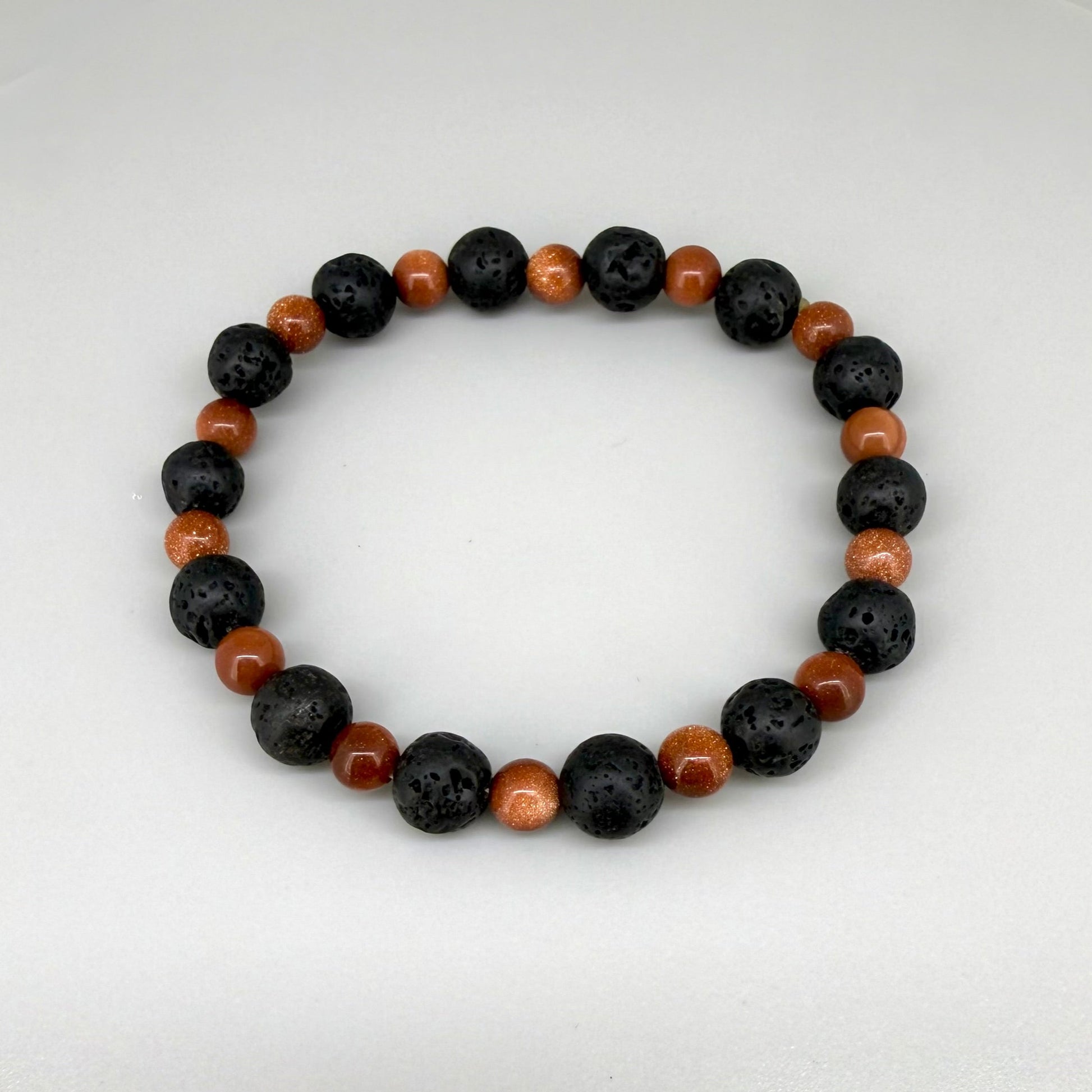 Lava and goldstone beaded bracelet, 18cm, alternating matte black lava beads and smaller shimmering golden-brown man-made goldstone beads on elastic stretch band.