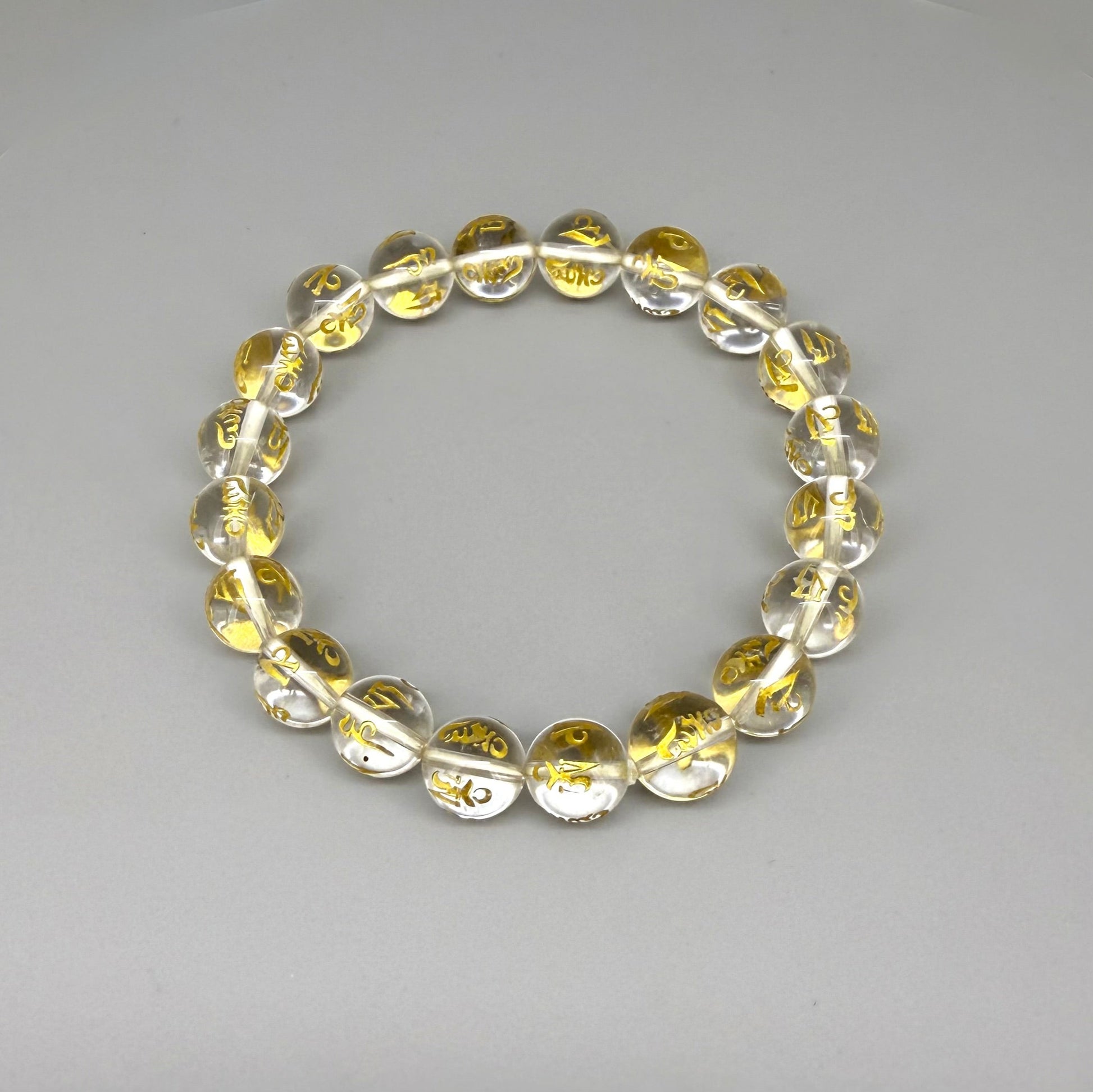 Clear quartz beaded bracelet, 19cm, transparent gemstone beads engraved with golden Sanskrit mantra Om Mani Padme Hum on elastic stretch band.