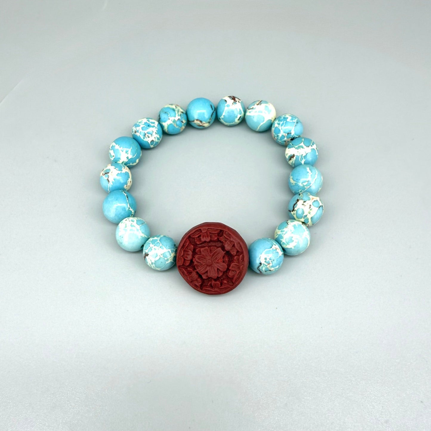 Varescite beaded bracelet, 18cm, turquoise-green gemstone beads with carved red cinnabar-style accent bead on elastic stretch band.