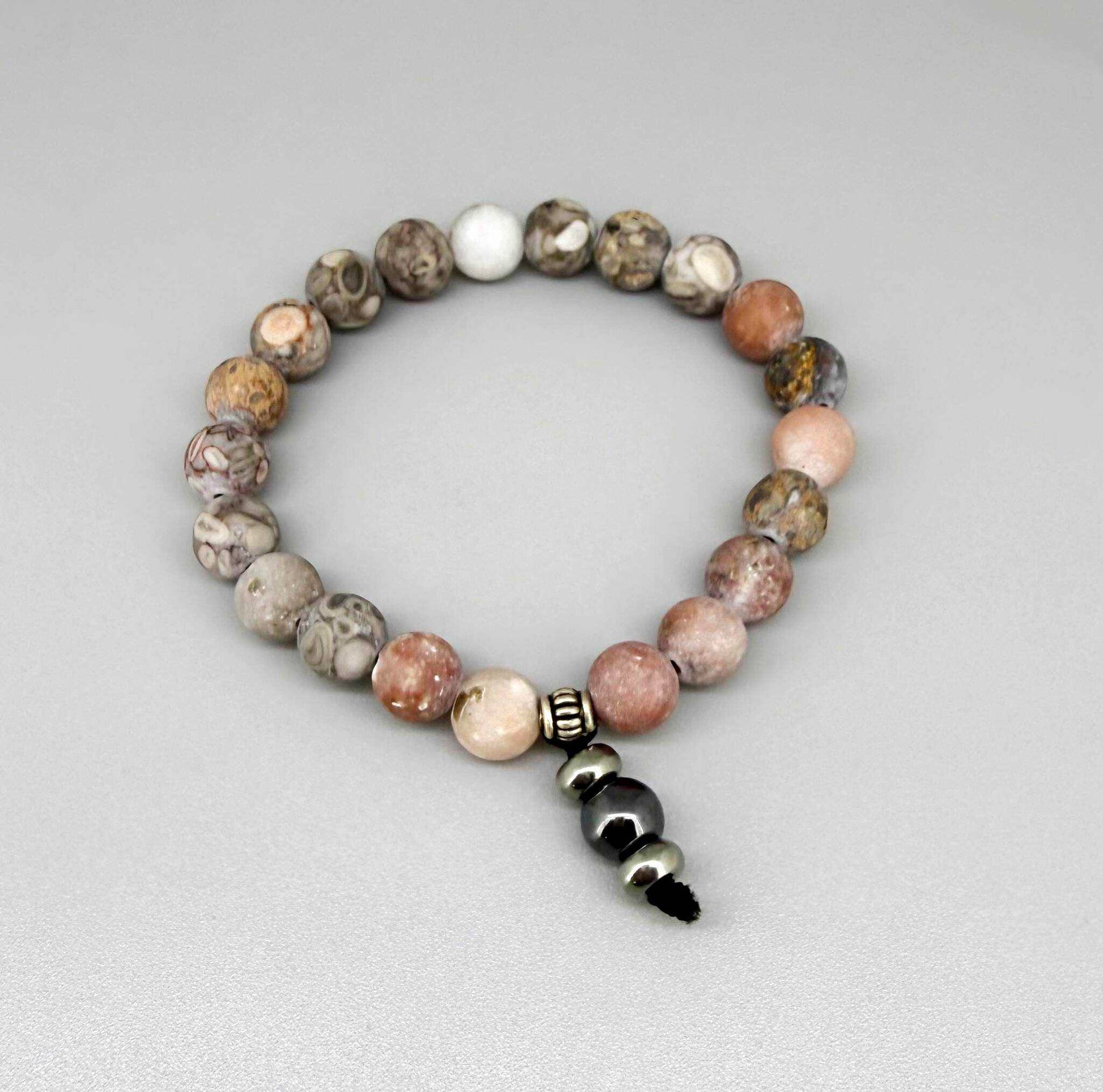 Maifanite mala bracelet with natural earthy-toned beads in beige, grey and soft terracotta shades, featuring a subtle charm detail.