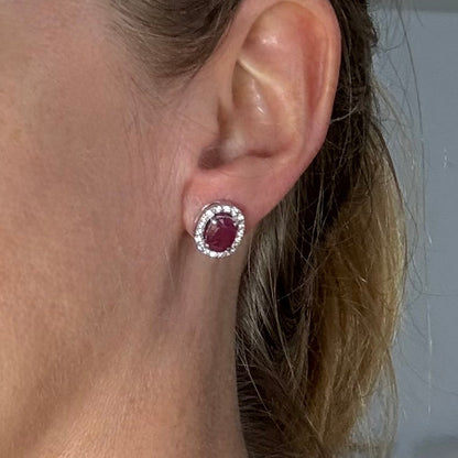 White gold plated sterling silver stud earrings with 2.6 ct natural rubies surrounded by cubic zirconia; classic halo design, elegant brilliance.