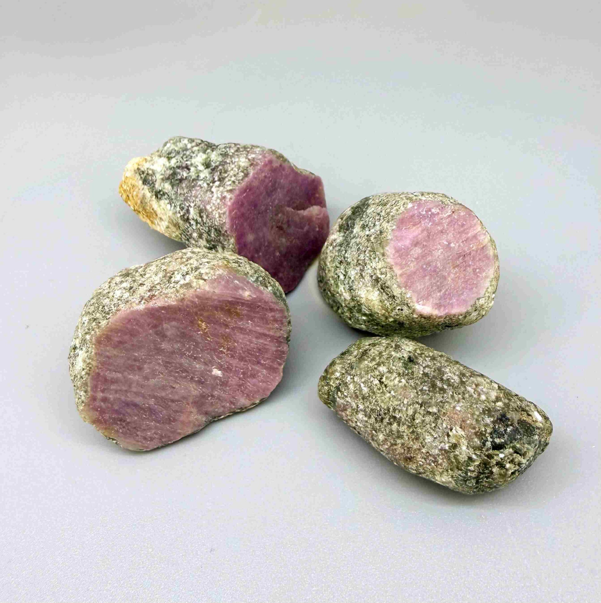 Natural ruby in grey-green host rock, uncut rough stones with pink to purplish-pink ruby sections.