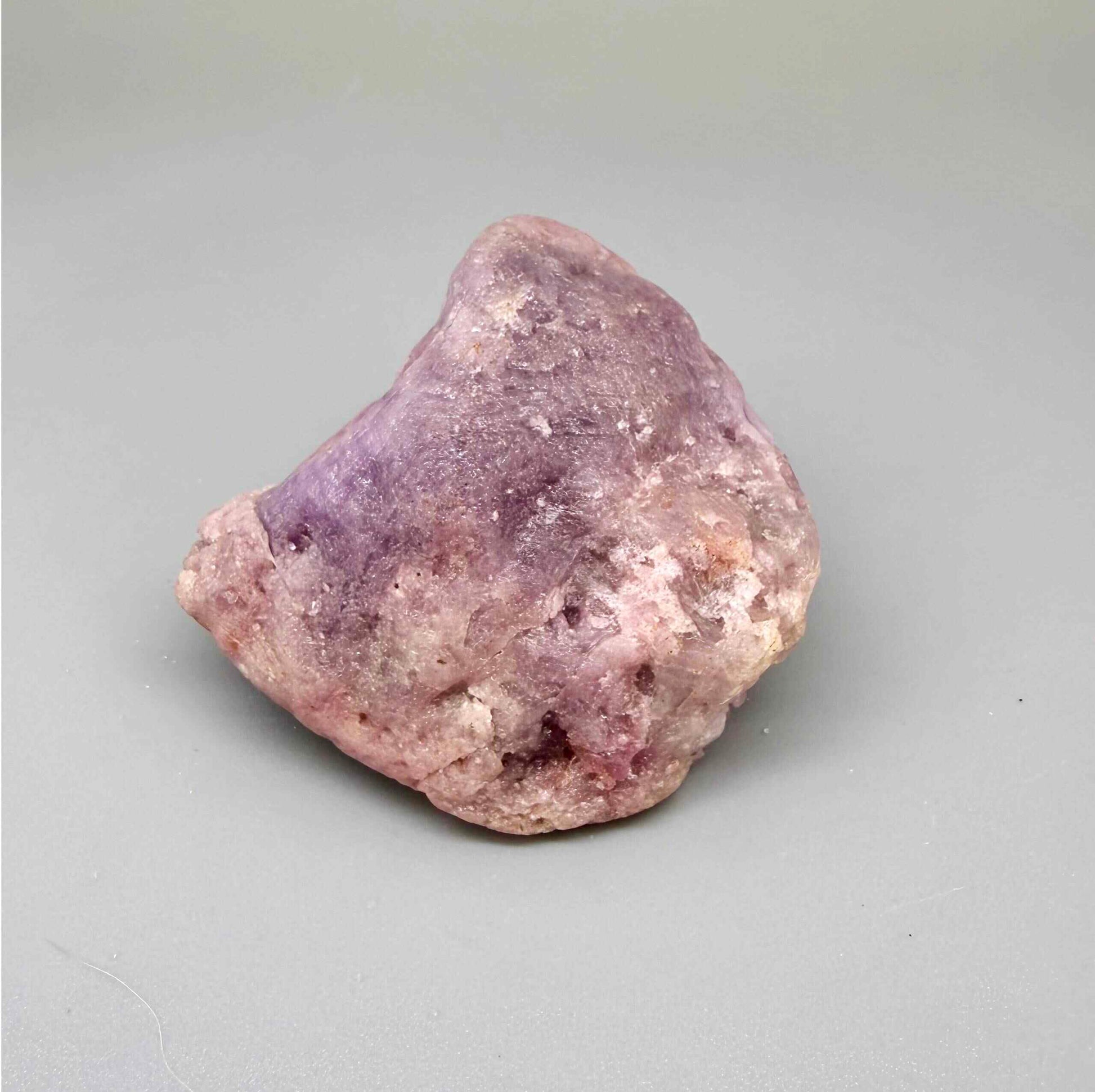 Natural ruby rough stone in lilac to lavender-pink tones, uncut corundum specimen photographed on neutral background.