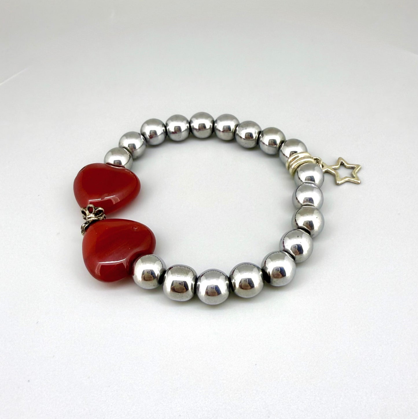 Silver hematite beaded bracelet, 18cm, metallic gemstone beads with two orange-red heart-shaped carnelian accents on elastic stretch band.