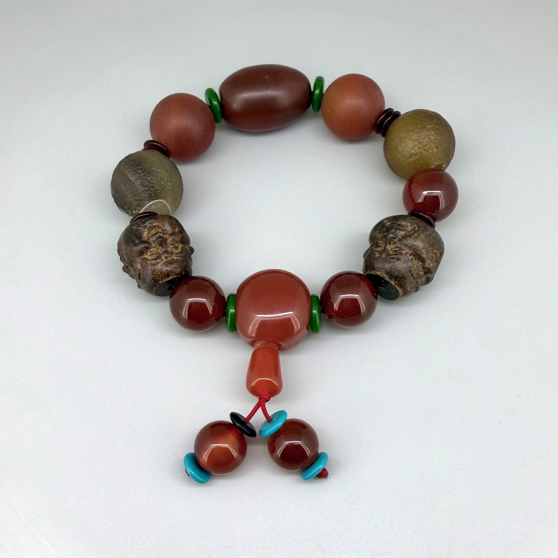 Carnelian and agate beaded bracelet, 20cm, orange-red and brown gemstone beads with two carved wooden head accents on elastic stretch band.