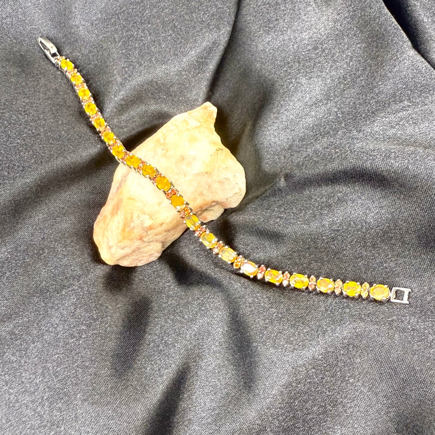 White gold plated sapphire bracelet in yellow, orange, and red hues on neutral background