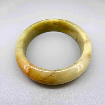 Polished jade bangle in soft earth tones with smooth surface and natural variations
