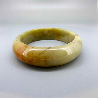 Polished jade bangle in soft earth tones with smooth surface and natural variations