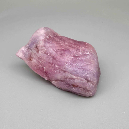 Natural ruby rough stone in soft pink to pale rose tones, uncut corundum specimen photographed on neutral background.